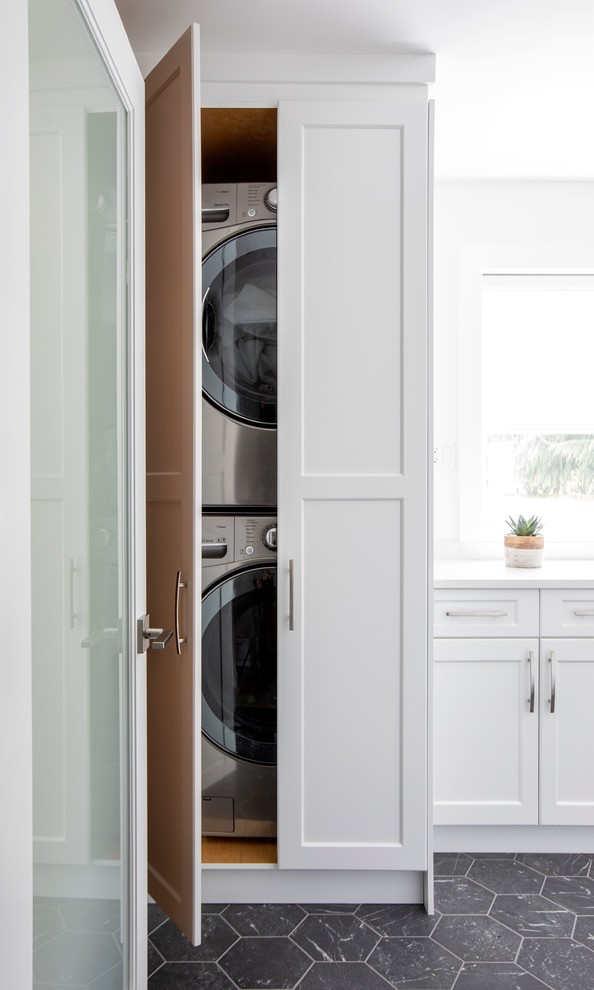 Design ideas for a mid-sized contemporary single-wall dedicated laundry room in Vancouver with white cabinets, white walls, a stacked washer and dryer, black floor, white benchtop, recessed-panel cabinets, quartz benchtops and marble floors.