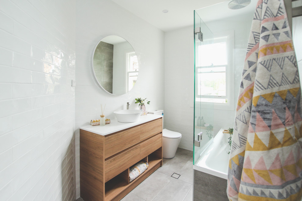 This is an example of a mid-sized scandinavian master bathroom in Sydney with medium wood cabinets, a drop-in tub, a shower/bathtub combo, a two-piece toilet, white tile, white walls, porcelain floors, a console sink, grey floor, a hinged shower door, white benchtops, a single vanity and a freestanding vanity.