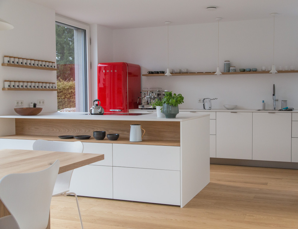 Contemporary galley kitchen in Munich with an undermount sink, flat-panel cabinets, white cabinets, coloured appliances, medium hardwood floors, a peninsula, brown floor and white benchtop.