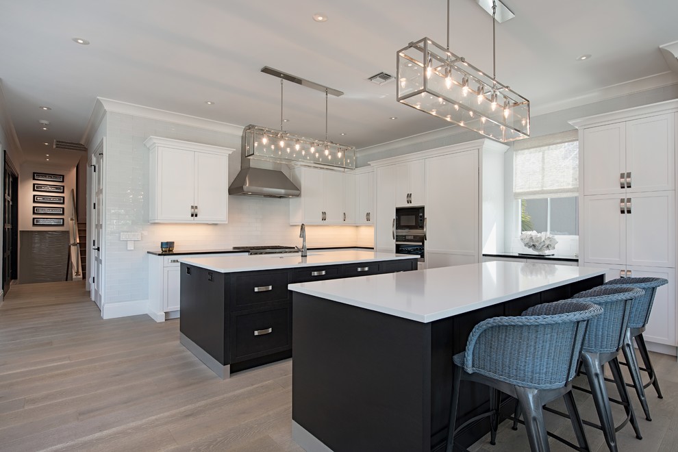 Eat-in kitchen - transitional l-shaped light wood floor and beige floor eat-in kitchen idea in Denver with an undermount sink, shaker cabinets, black cabinets, white backsplash, stainless steel appliances, two islands and white countertops