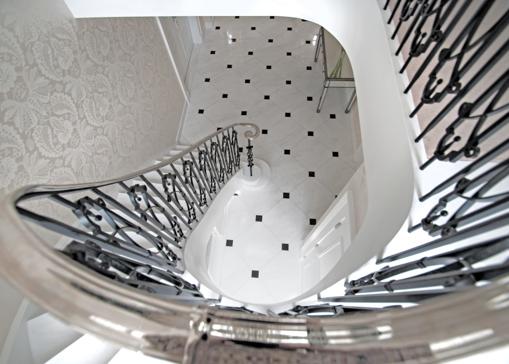 Imagen de escalera curva tradicional grande con escalones de mármol, contrahuellas de mármol y barandilla de metal