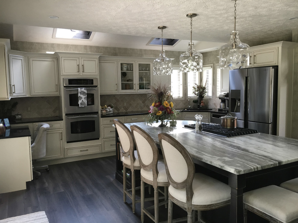 Example of a large transitional u-shaped laminate floor and gray floor eat-in kitchen design with an undermount sink, recessed-panel cabinets, white cabinets, granite countertops, white backsplash, ceramic backsplash, stainless steel appliances, an island and black countertops