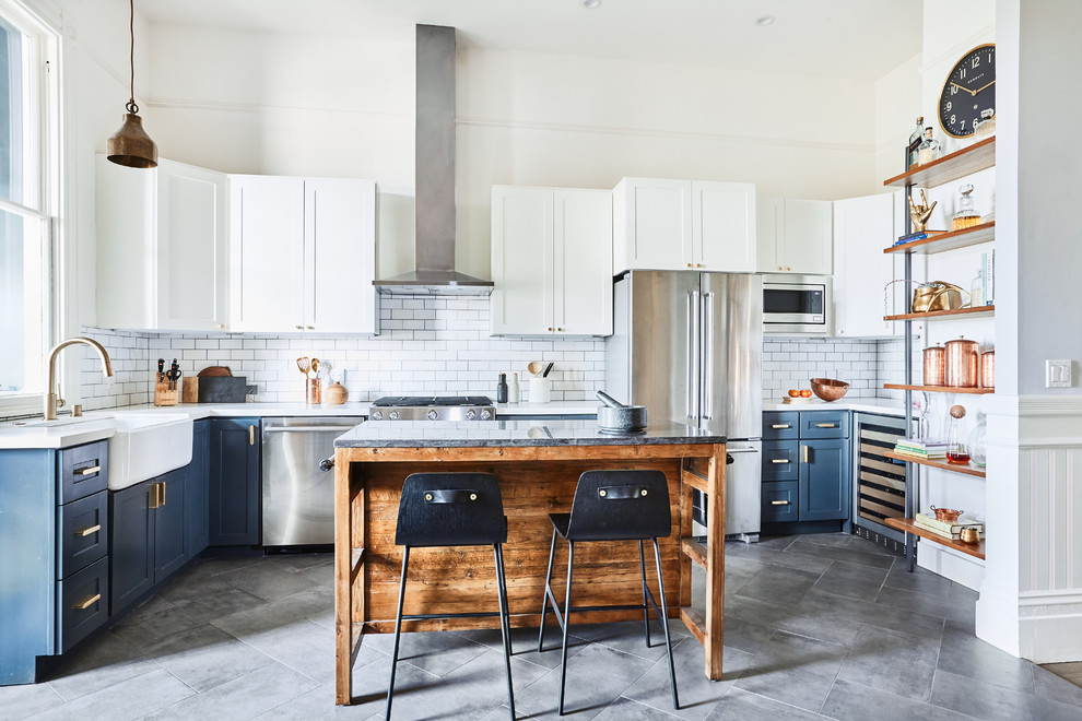 Design ideas for a mid-sized traditional l-shaped eat-in kitchen in San Francisco with a farmhouse sink, shaker cabinets, white cabinets, quartz benchtops, white splashback, ceramic splashback, stainless steel appliances, slate floors, with island, grey floor and white benchtop.