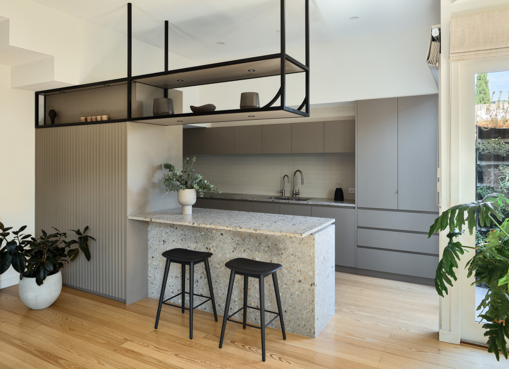 Inspiration for a small contemporary kitchen/diner in Melbourne with a double-bowl sink, flat-panel cabinets, grey cabinets, terrazzo worktops, grey splashback, ceramic splashback, black appliances, light hardwood flooring, an island and multicoloured worktops.