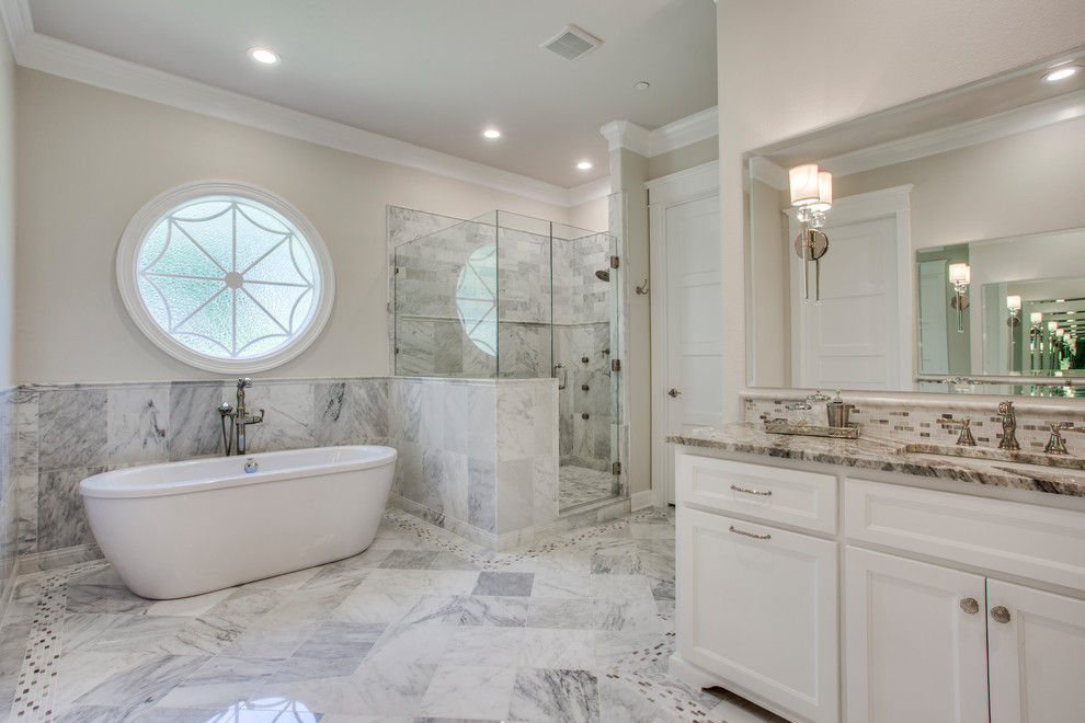 Design ideas for a large transitional master bathroom in Dallas with recessed-panel cabinets, white cabinets, a freestanding tub, a corner shower, gray tile, white tile, marble, beige walls, marble floors, an undermount sink, granite benchtops, green floor, a hinged shower door and brown benchtops.