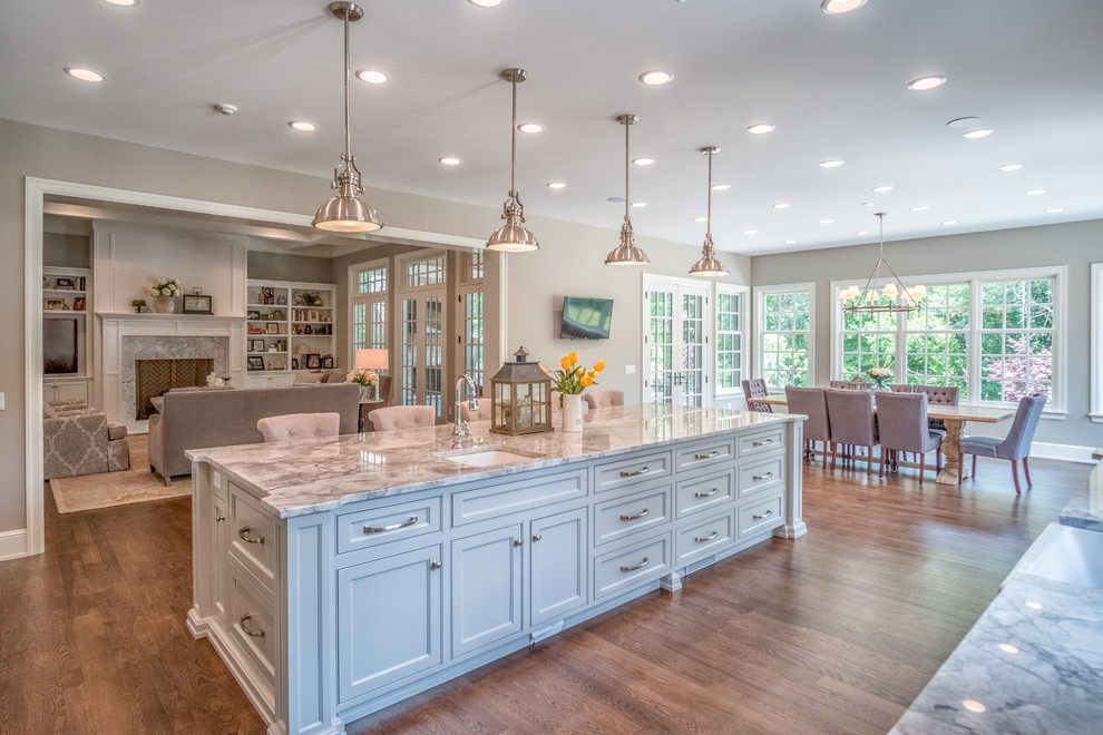 Example of a large transitional l-shaped medium tone wood floor eat-in kitchen design with a farmhouse sink, shaker cabinets, white cabinets, white backsplash, subway tile backsplash, stainless steel appliances, an island and marble countertops