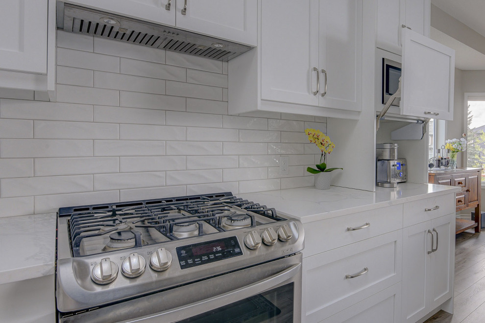 Photo of a mid-sized transitional l-shaped eat-in kitchen in Calgary with an undermount sink, shaker cabinets, grey cabinets, quartz benchtops, white splashback, subway tile splashback, stainless steel appliances, vinyl floors, with island, grey floor and white benchtop.