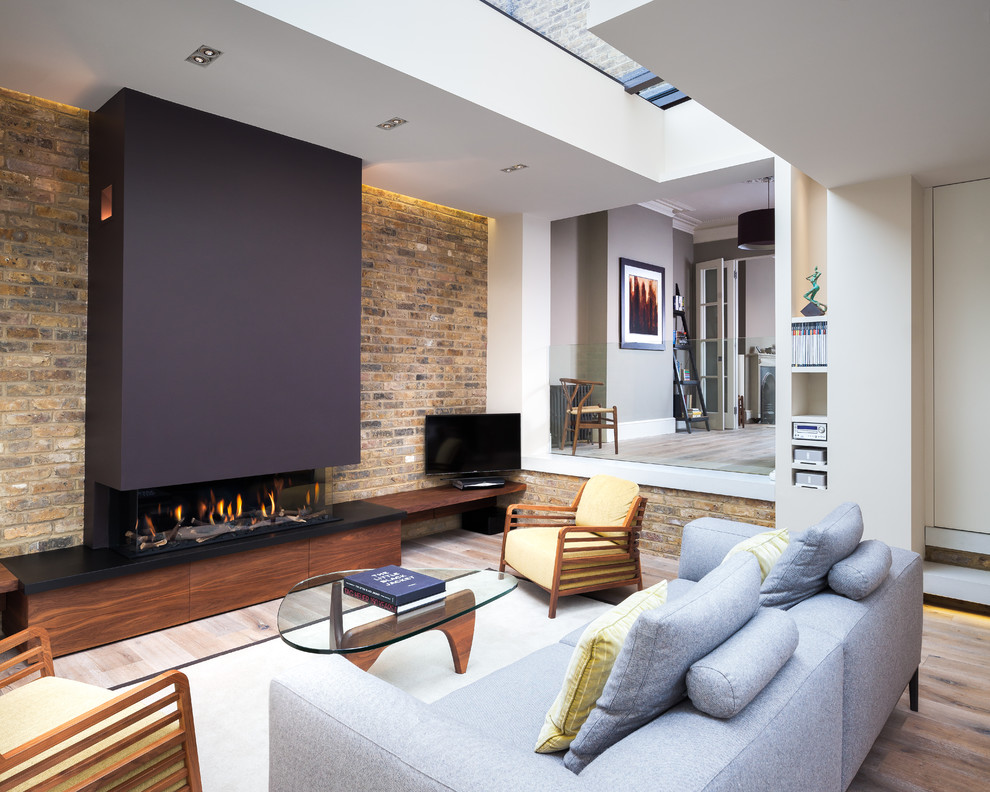 Design ideas for a mid-sized contemporary enclosed living room in London with white walls, light hardwood floors, a two-sided fireplace, a freestanding tv and beige floor.