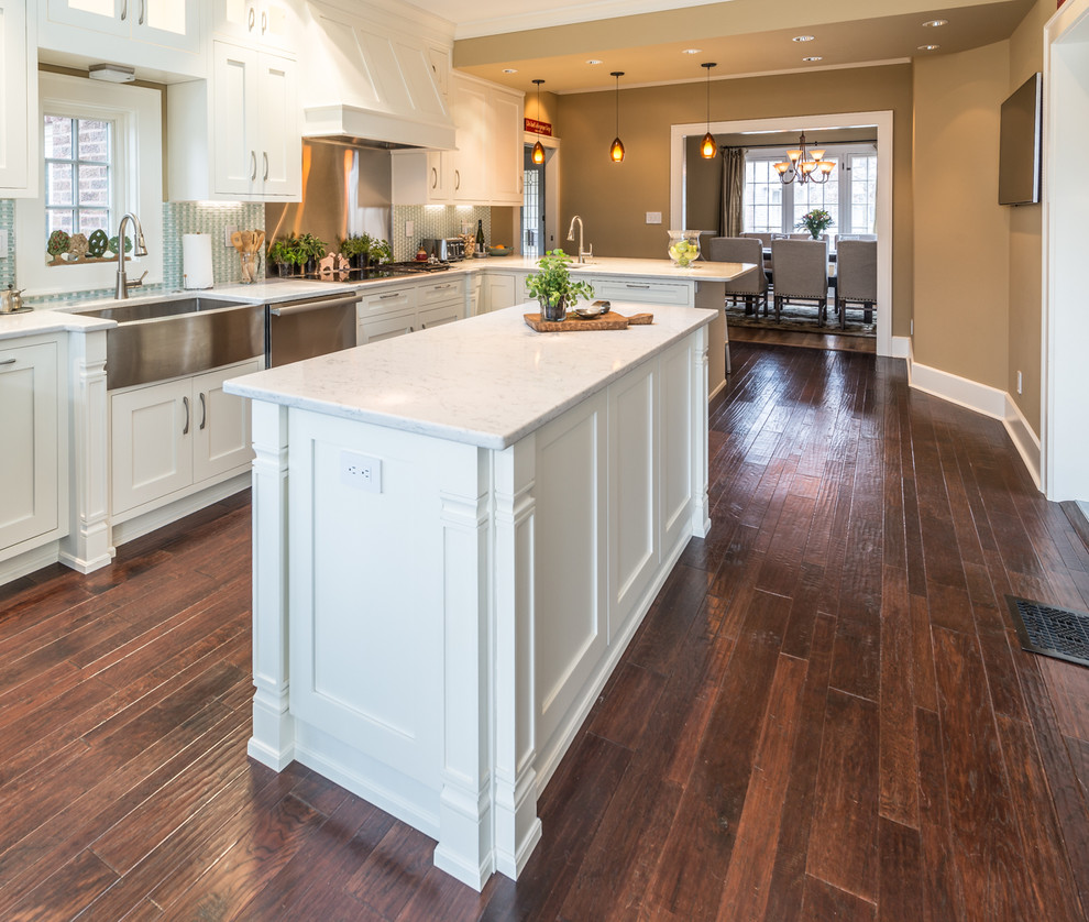 Photo of a large transitional l-shaped eat-in kitchen in Indianapolis with a farmhouse sink, shaker cabinets, white cabinets, quartz benchtops, blue splashback, mosaic tile splashback, stainless steel appliances, medium hardwood floors and a peninsula.