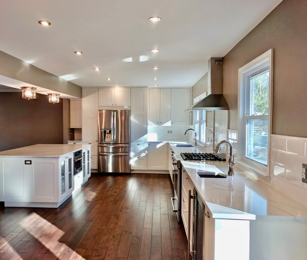 Large classic l-shaped kitchen/diner in Seattle with a submerged sink, white cabinets, engineered stone countertops, white splashback, ceramic splashback, stainless steel appliances, medium hardwood flooring, an island and white worktops.