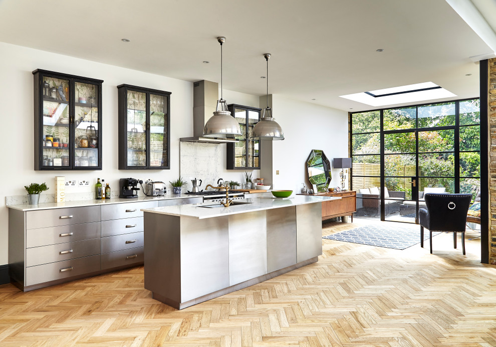 This is an example of a contemporary galley open plan kitchen in London with an undermount sink, flat-panel cabinets, stainless steel cabinets, light hardwood floors, with island, beige floor and white benchtop.