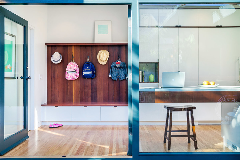 This is an example of a midcentury mudroom in San Francisco with white walls, light hardwood floors and a glass front door.
