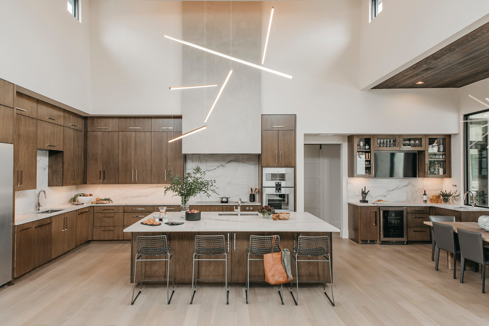 This is an example of an expansive contemporary l-shaped eat-in kitchen in Austin with a single-bowl sink, flat-panel cabinets, medium wood cabinets, quartzite benchtops, white splashback, stone slab splashback, stainless steel appliances, light hardwood floors, with island and white benchtop.