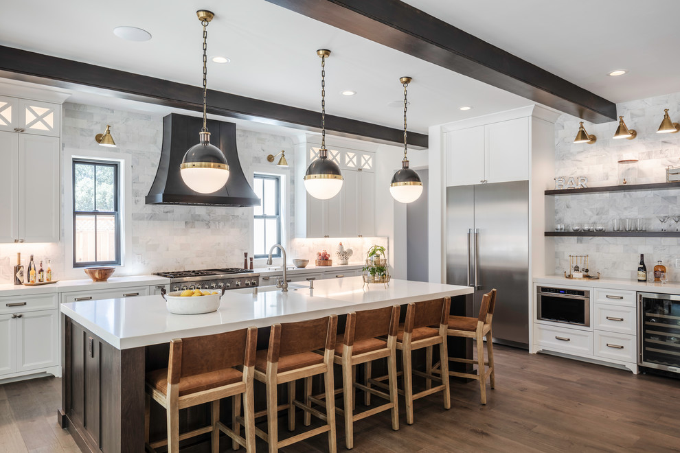 Large transitional l-shaped open plan kitchen in San Francisco with a farmhouse sink, shaker cabinets, white cabinets, quartz benchtops, grey splashback, marble splashback, stainless steel appliances, medium hardwood floors, with island, brown floor and white benchtop.