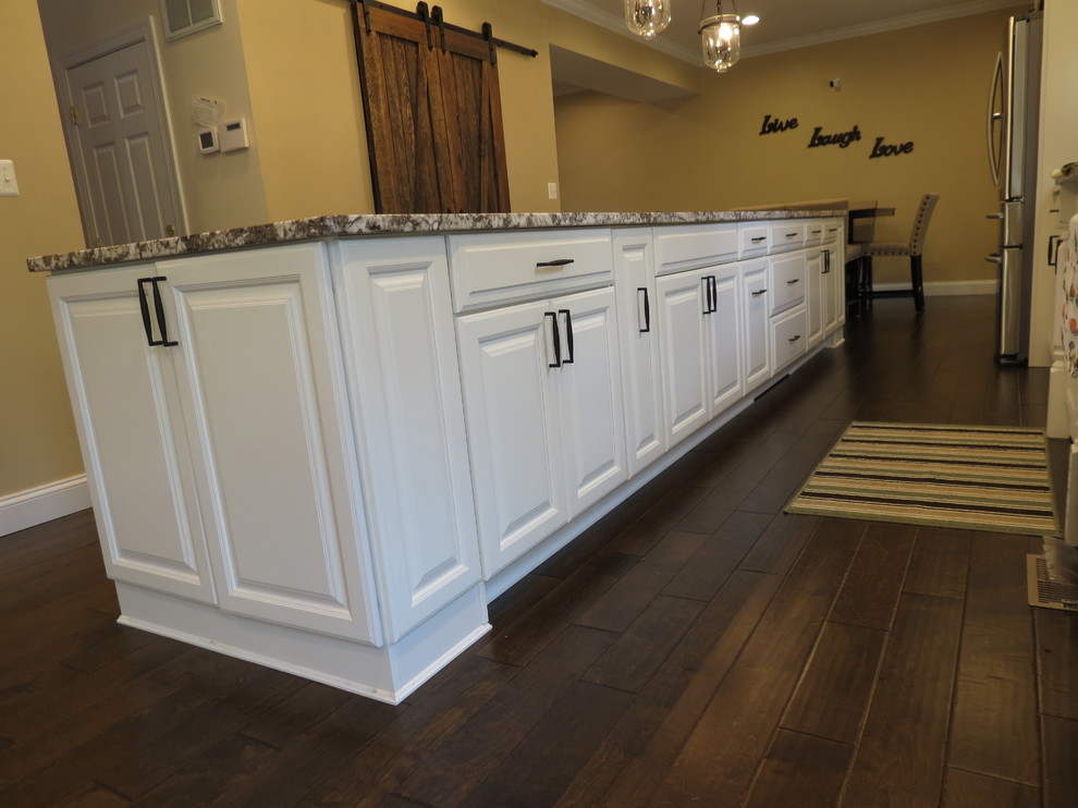 Example of a large transitional galley dark wood floor and brown floor kitchen design with a double-bowl sink, raised-panel cabinets, white cabinets, granite countertops, white backsplash, porcelain backsplash, stainless steel appliances and an island