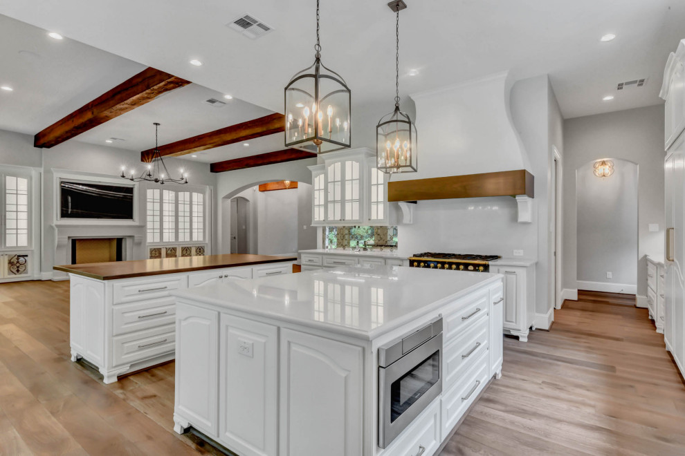 Large french country l-shaped medium tone wood floor and brown floor open concept kitchen photo in Houston with a farmhouse sink, raised-panel cabinets, white cabinets, white backsplash, mirror backsplash, two islands and white countertops