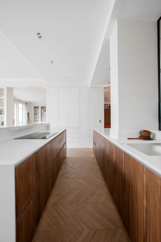 Inspiration for an expansive contemporary galley eat-in kitchen in Paris with an undermount sink, beaded inset cabinets, white cabinets, solid surface benchtops, white splashback, light hardwood floors, with island and white benchtop.