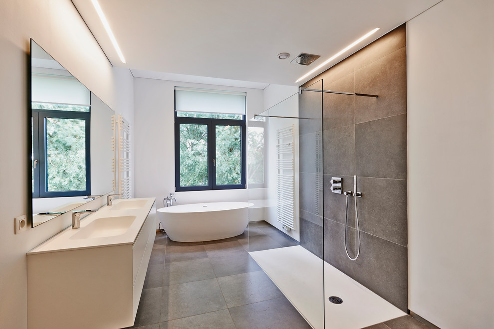 Design ideas for a mid-sized contemporary master bathroom in Dijon with white cabinets, a drop-in tub, an open shower, a wall-mount toilet, gray tile, ceramic tile, white walls, ceramic floors, a console sink, onyx benchtops, grey floor, a shower curtain and white benchtops.