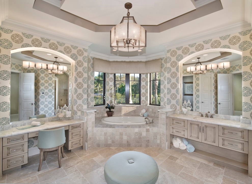 Photo of a large mediterranean master bathroom in Miami with an undermount sink, recessed-panel cabinets, multi-coloured walls, a drop-in tub, beige cabinets, travertine floors, marble benchtops, a corner shower and beige floor.