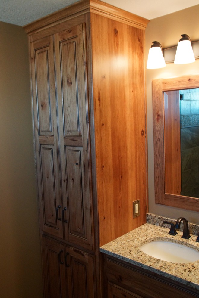 Inspiration for a mid-sized rustic master multicolored tile and stone tile travertine floor alcove shower remodel with raised-panel cabinets, medium tone wood cabinets, a one-piece toilet, beige walls, an undermount sink and granite countertops