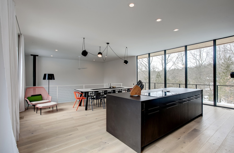 Mid-sized modern galley open plan kitchen in Grand Rapids with flat-panel cabinets, black cabinets, quartz benchtops, light hardwood floors, with island and beige floor.