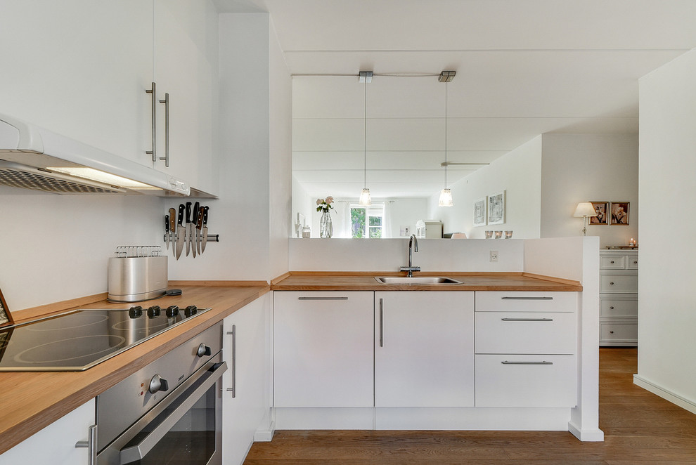 Design ideas for a mid-sized contemporary l-shaped separate kitchen in Copenhagen with a drop-in sink, flat-panel cabinets, white cabinets, wood benchtops, stainless steel appliances, light hardwood floors and no island.