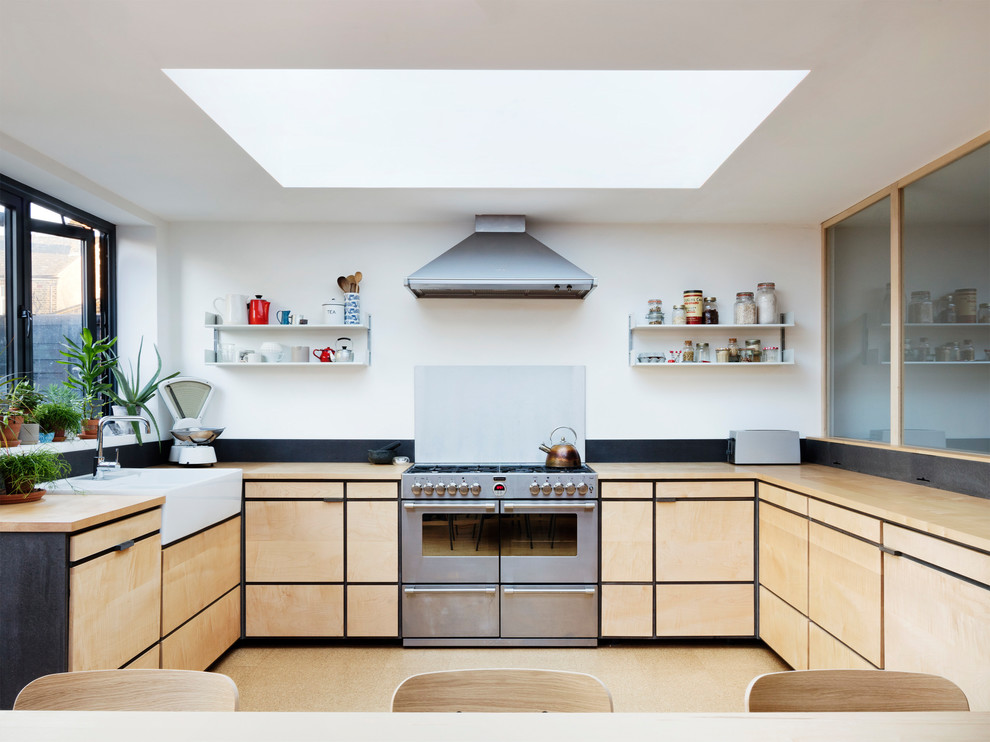 Scandinavian l-shaped eat-in kitchen in London with a farmhouse sink, flat-panel cabinets, light wood cabinets, wood benchtops, stainless steel appliances, cork floors, beige floor and no island.