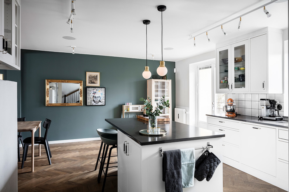 Photo of a large scandinavian u-shaped eat-in kitchen in Gothenburg with white cabinets, solid surface benchtops, white splashback, ceramic splashback, stainless steel appliances, dark hardwood floors, with island, brown floor and black benchtop.