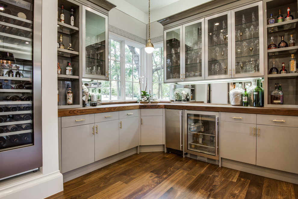 Transitional l-shaped wet bar in Dallas with flat-panel cabinets, grey cabinets, wood benchtops, mirror splashback, dark hardwood floors, brown floor and brown benchtop.