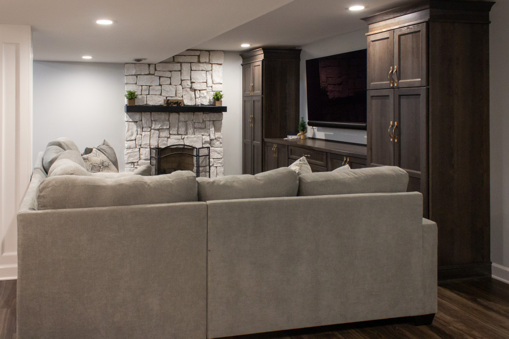 Inspiration for a mid-sized transitional fully buried basement in Chicago with a home bar, grey walls, vinyl floors, a standard fireplace, a stone fireplace surround and brown floor.