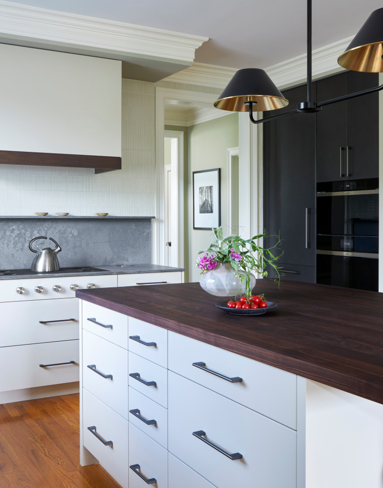 Inredning av ett modernt mellanstort grå grått kök, med en enkel diskho, släta luckor, vita skåp, grått stänkskydd, mellanmörkt trägolv, en köksö, brunt golv och träbänkskiva