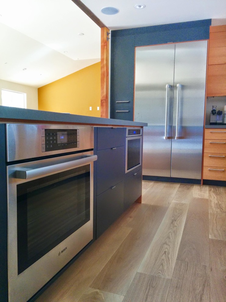 Photo of a mid-sized contemporary l-shaped eat-in kitchen in San Francisco with flat-panel cabinets, medium wood cabinets, quartzite benchtops, stainless steel appliances, light hardwood floors, with island, an undermount sink and black benchtop.
