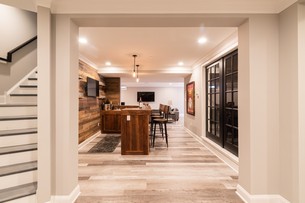 Large country fully buried basement in Philadelphia with a home bar, grey walls, grey floor and planked wall panelling.