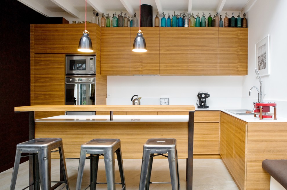 This is an example of a mid-sized contemporary l-shaped eat-in kitchen in Paris with with island, an undermount sink, beaded inset cabinets, medium wood cabinets, quartz benchtops, white splashback, panelled appliances and concrete floors.