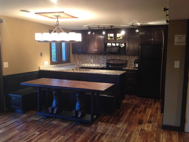 Eat-in kitchen - small rustic galley medium tone wood floor and brown floor eat-in kitchen idea with an undermount sink, shaker cabinets, dark wood cabinets, granite countertops, brown backsplash, glass tile backsplash, black appliances and a peninsula