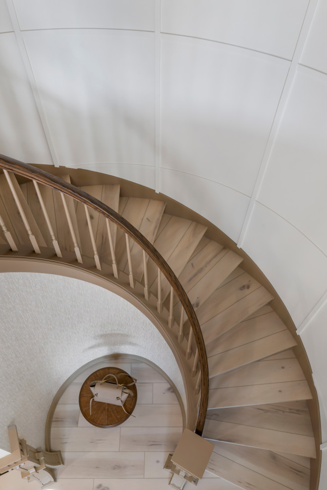 Стильный дизайн: большая изогнутая деревянная лестница в классическом стиле с деревянными ступенями, деревянными перилами и панелями на стенах - последний тренд