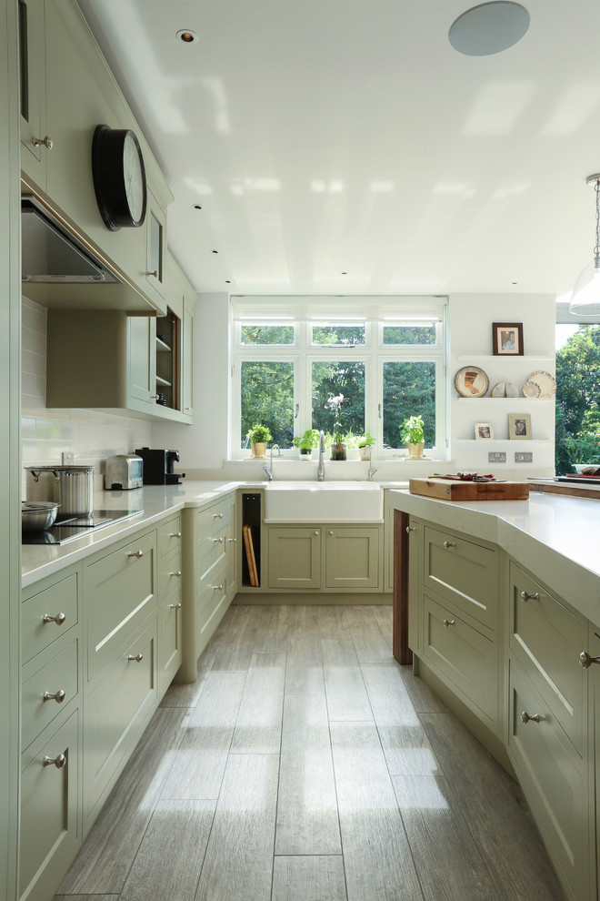 Photo of a large traditional u-shaped kitchen in London with a farmhouse sink, shaker cabinets, white splashback and with island.