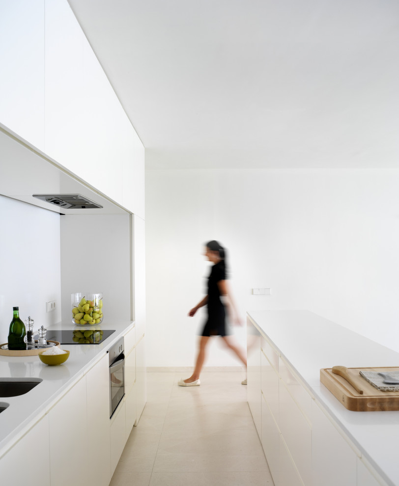 Inspiration for a small modern galley kitchen in Valencia with an undermount sink, flat-panel cabinets, white cabinets, with island, solid surface benchtops, white splashback and ceramic floors.