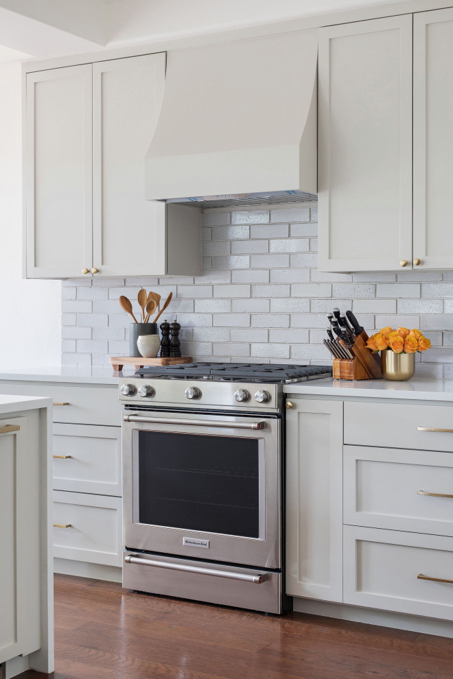 Open concept kitchen - mid-sized transitional medium tone wood floor and brown floor open concept kitchen idea in Austin with an undermount sink, shaker cabinets, gray cabinets, quartz countertops, white backsplash, brick backsplash, stainless steel appliances, a peninsula and white countertops