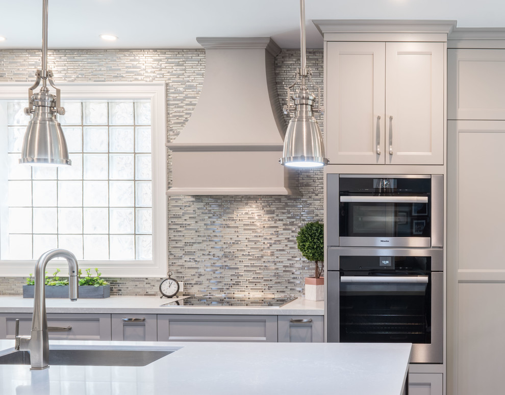 Mid-sized transitional l-shaped kitchen pantry in Toronto with an undermount sink, shaker cabinets, grey cabinets, quartz benchtops, white splashback, mosaic tile splashback, stainless steel appliances, porcelain floors, with island, beige floor and white benchtop.