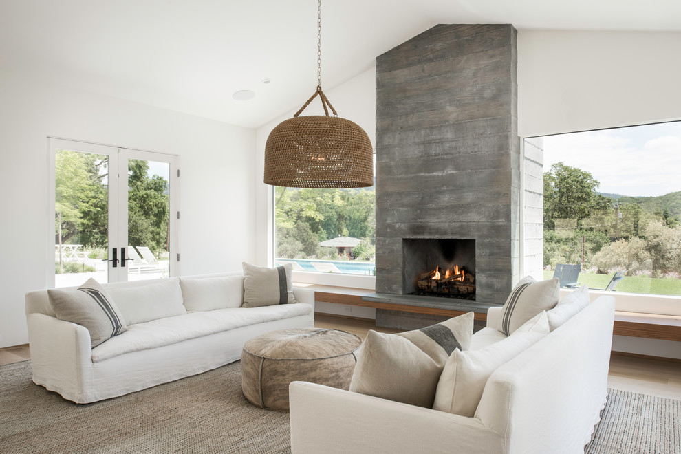 Country open concept living room in San Francisco with white walls, light hardwood floors, a standard fireplace, a concrete fireplace surround and beige floor.
