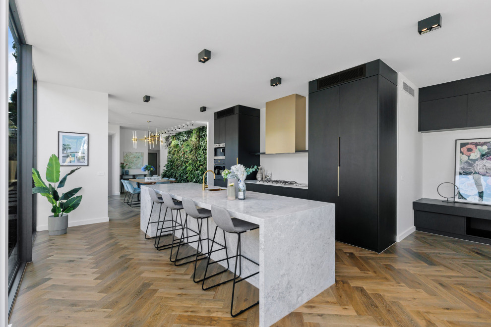Photo of a contemporary galley kitchen in Melbourne with an undermount sink, flat-panel cabinets, black cabinets, panelled appliances, dark hardwood floors, with island, brown floor and grey benchtop.