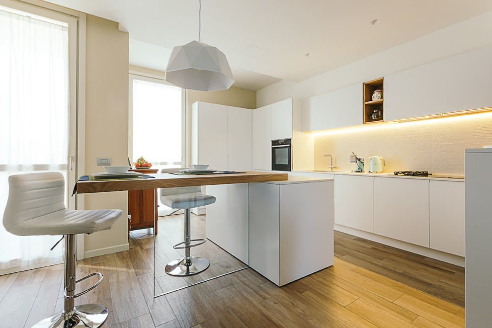 Design ideas for a contemporary l-shaped eat-in kitchen in Other with white cabinets, white splashback, with island, an undermount sink, flat-panel cabinets, panelled appliances, medium hardwood floors, brown floor and white benchtop.