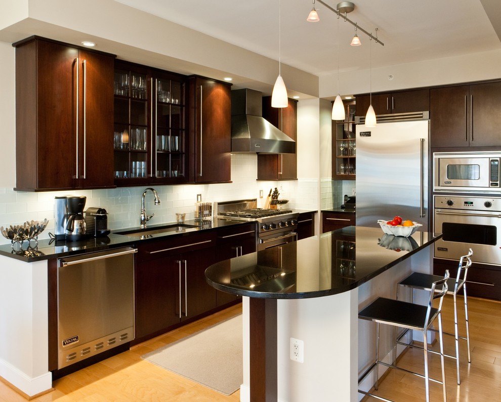 Example of a transitional l-shaped light wood floor kitchen design in DC Metro with an undermount sink, flat-panel cabinets, dark wood cabinets, white backsplash, subway tile backsplash, stainless steel appliances and an island