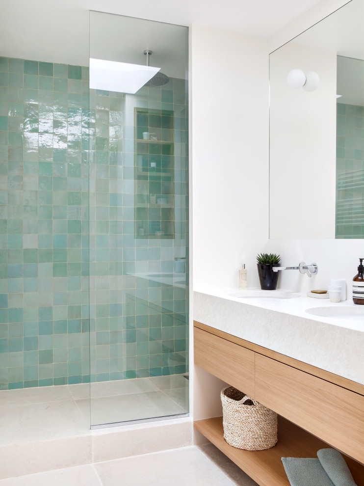 Cette image montre une salle d'eau design en bois clair de taille moyenne avec un placard à porte affleurante, une douche à l'italienne, un carrelage vert, du carrelage en travertin, un plan de toilette beige, meuble double vasque et meuble-lavabo suspendu.