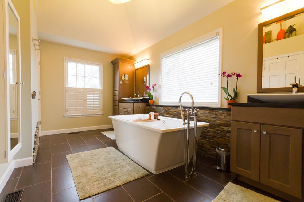 Photo of an expansive contemporary master bathroom in St Louis with shaker cabinets, medium wood cabinets, a freestanding tub, an alcove shower, a two-piece toilet, multi-coloured tile, stone tile, green walls, porcelain floors, a vessel sink, engineered quartz benchtops, brown floor and a hinged shower door.