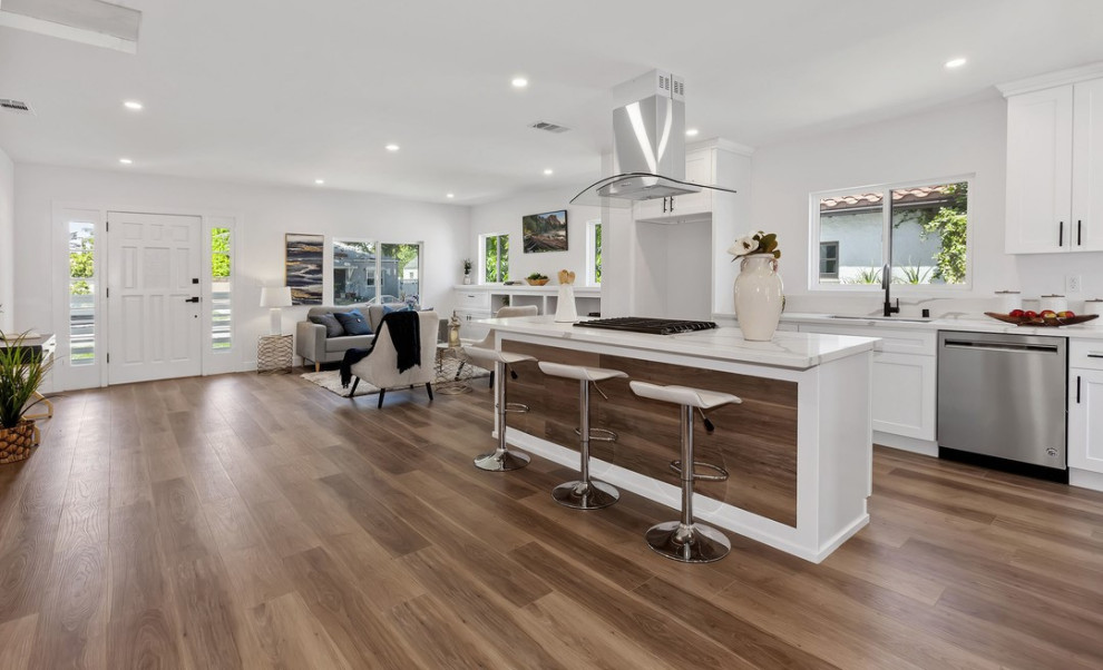 This is an example of a contemporary single-wall kitchen in Los Angeles with an undermount sink, shaker cabinets, white cabinets, marble benchtops, white splashback, ceramic splashback, stainless steel appliances, dark hardwood floors, with island, brown floor and white benchtop.