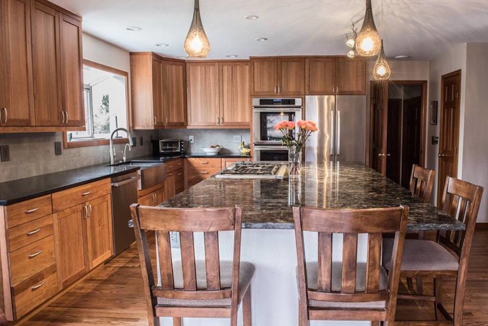 Eat-in kitchen - large transitional l-shaped dark wood floor eat-in kitchen idea in Denver with a farmhouse sink, shaker cabinets, medium tone wood cabinets, granite countertops, beige backsplash, stone tile backsplash, stainless steel appliances and an island