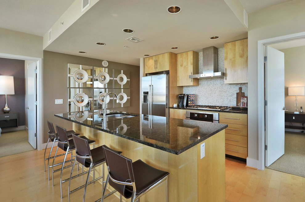 Small transitional galley light wood floor open concept kitchen photo in Austin with a double-bowl sink, flat-panel cabinets, light wood cabinets, granite countertops, beige backsplash, mosaic tile backsplash, stainless steel appliances and an island