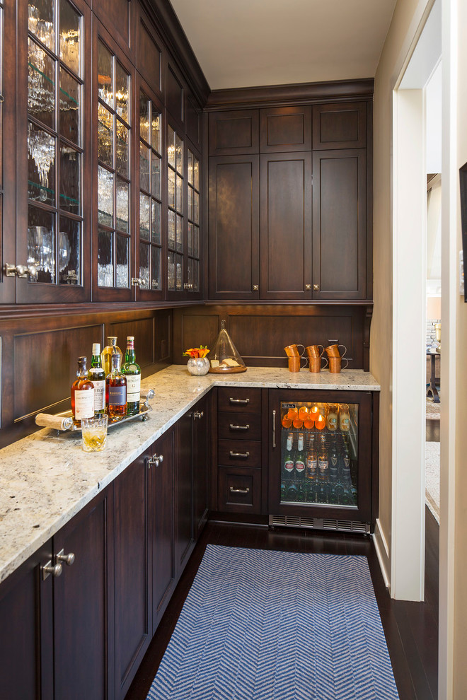 This is an example of a traditional l-shaped wet bar in Minneapolis with shaker cabinets, dark wood cabinets, granite benchtops, brown splashback, timber splashback and dark hardwood floors.